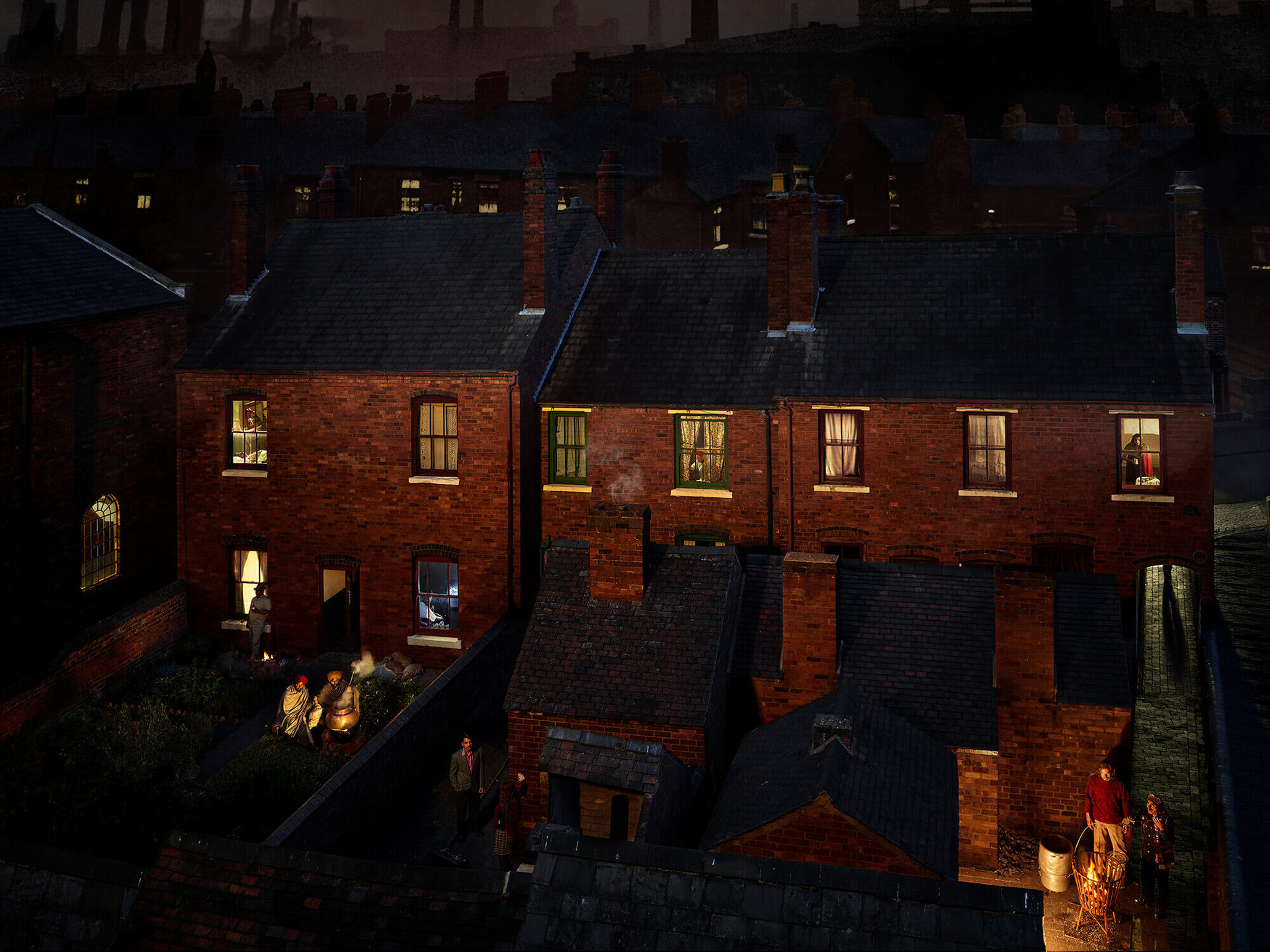 An elevated nighttime view across the rooftops of Black Country terrace houses. Factory chimneys rise against the sky. Warm light spills from windows. In the back yards below, small figures gather around a fire.