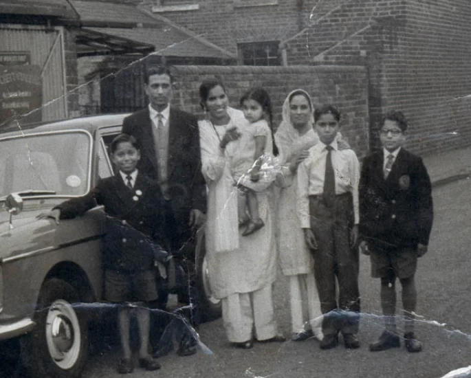 A Punjabi family pose beside their car outside a Black Country factory, 1960s