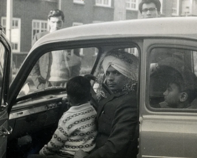 Young men in a car, one wearing a turban bandage, the lived reality of migration