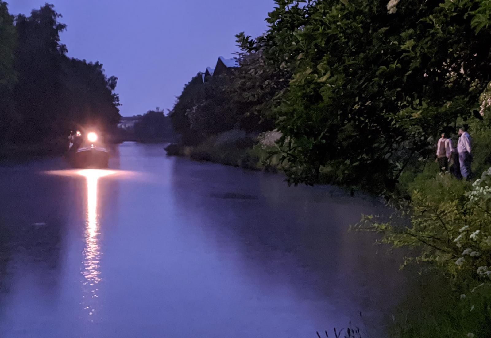 Canal at dusk with barge headlight approaching and cast on the towpath