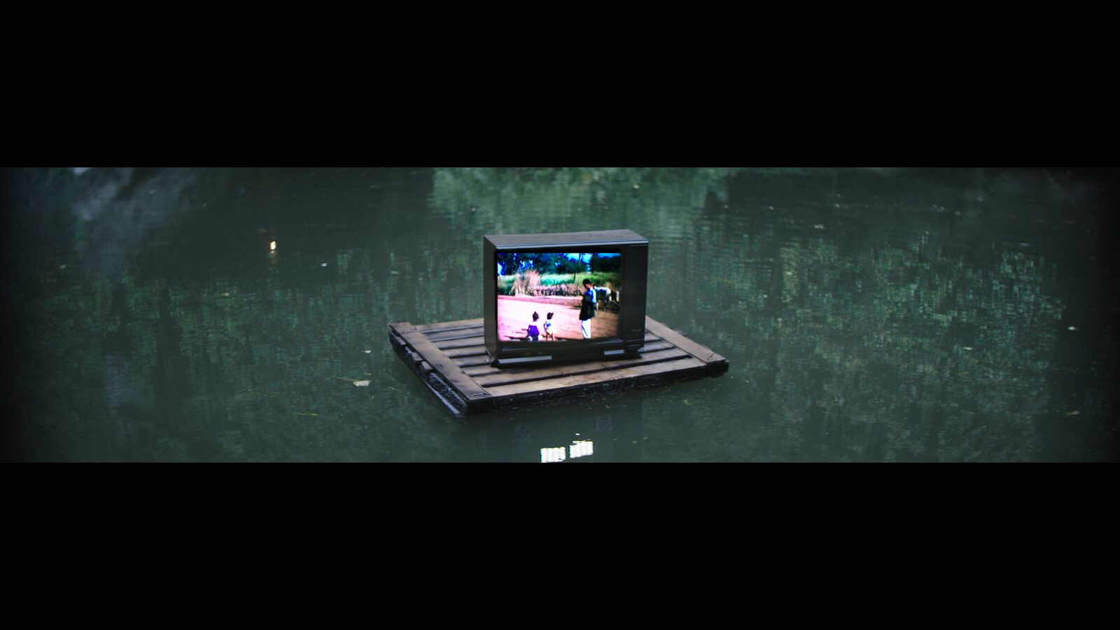 A vintage television floats on a wooden pallet along a canal — the imagined in-between world